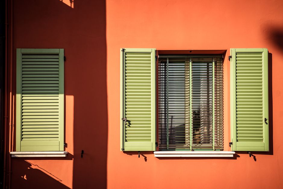 A modern exterior with green shutters against a vivid orange wall, showcasing contemporary design.